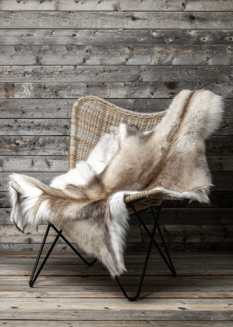 A light reindeer hide on a rattan chair in front of a weathered wooden wall